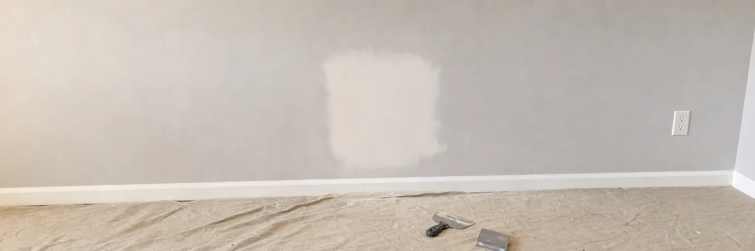 Patched and sanded section of wall above a dust sheet, with a taping knife beside it