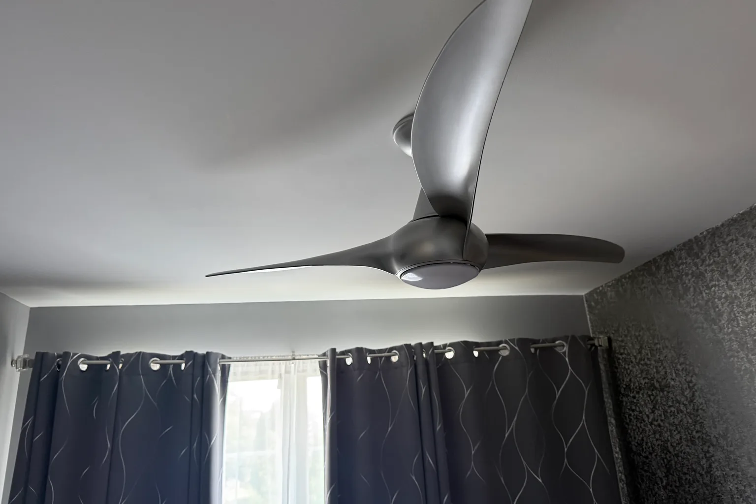 Newly installed three-blade ceiling fan viewed from below in a curtained bedroom