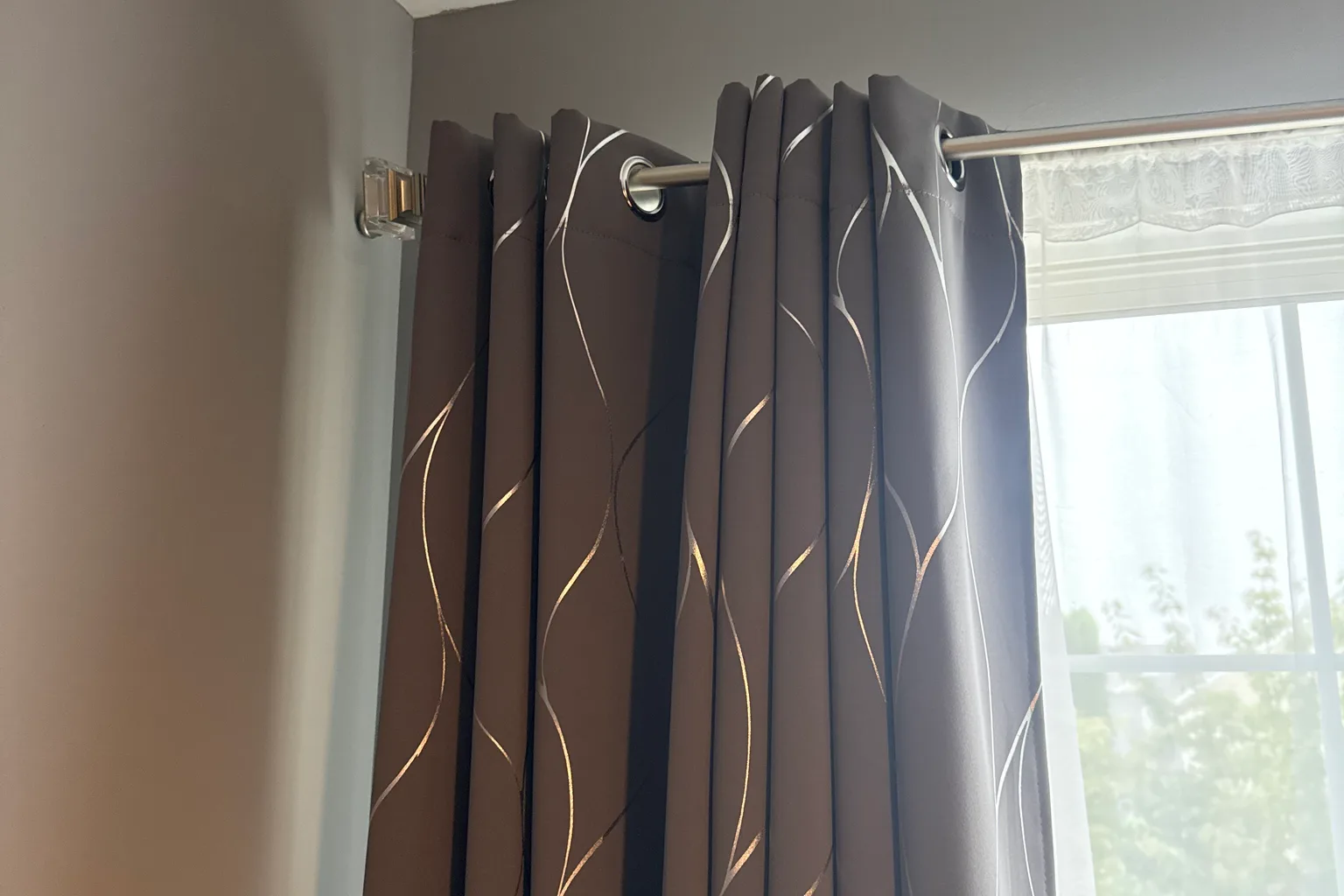 Curtain rod mounted level on its bracket carrying full-length grommet curtains beside a window