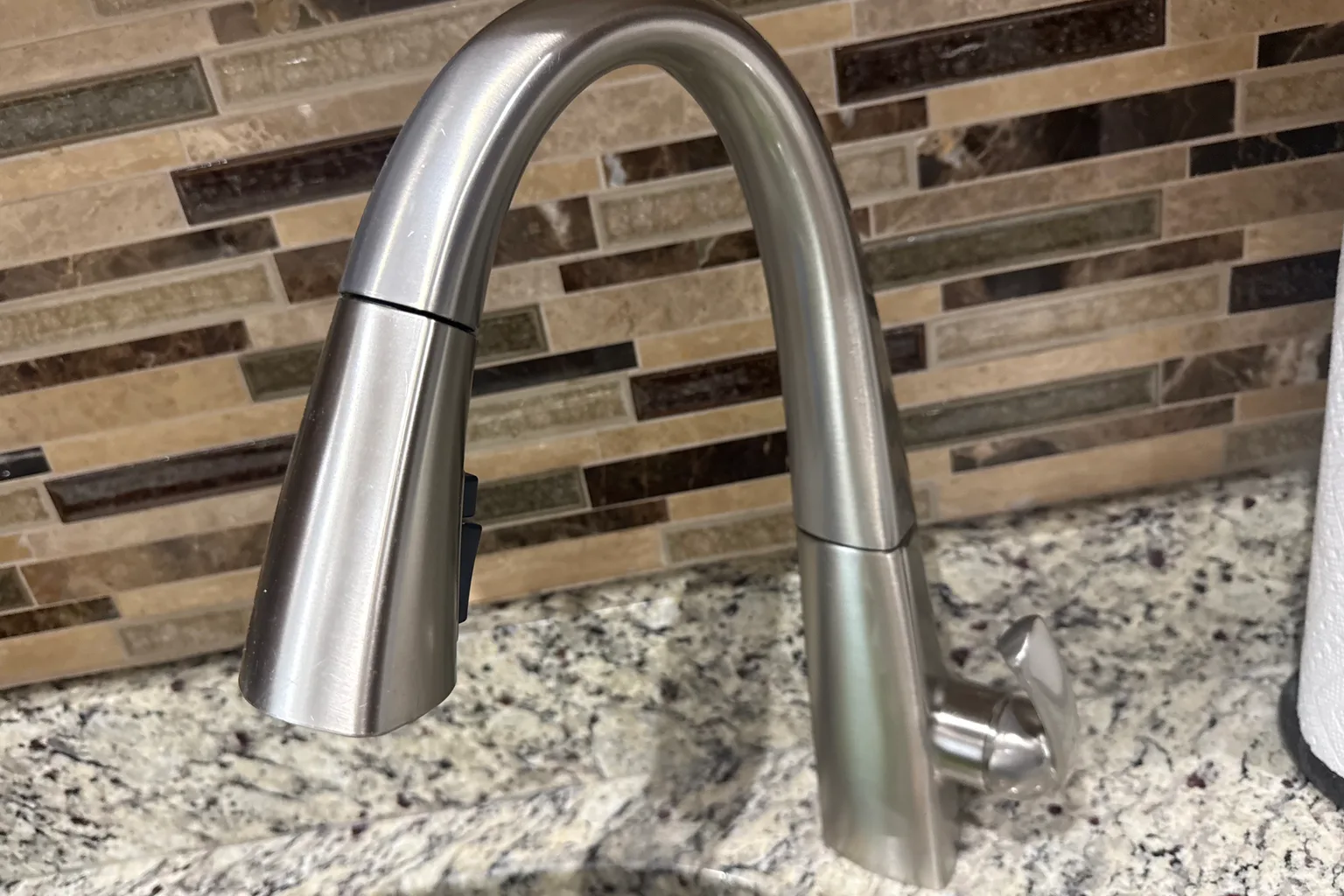 Newly installed brushed-nickel pull-down kitchen faucet against a mosaic tile backsplash