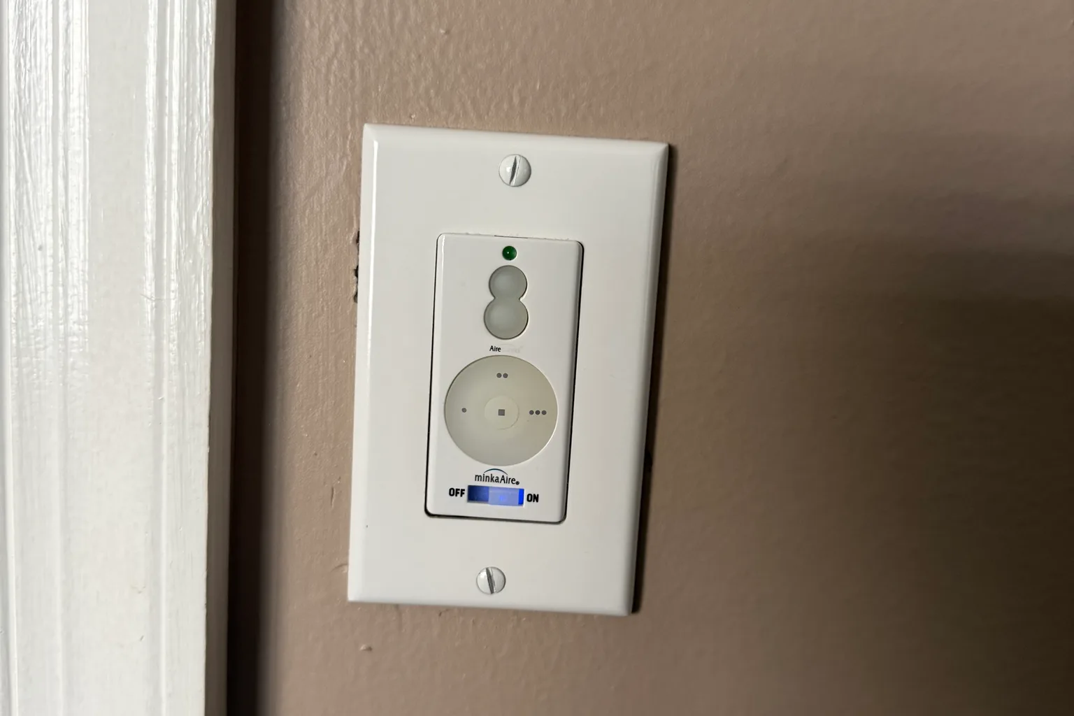 Newly fitted ceiling-fan wall control on a white plate beside a door frame