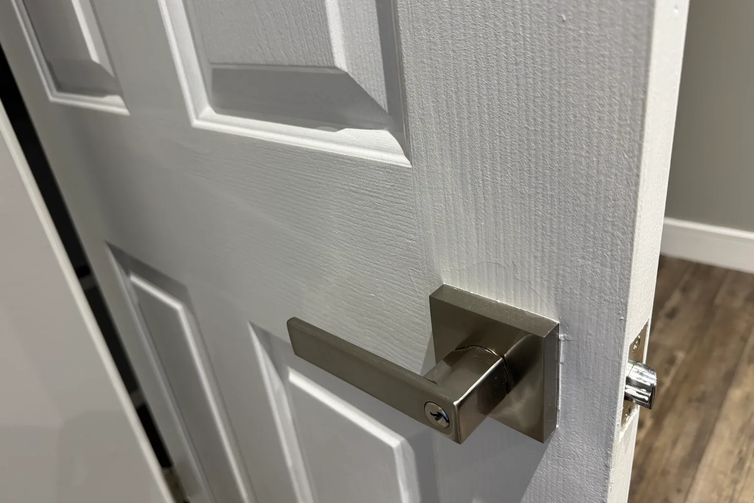 Newly installed satin-nickel lever handle and strike plate on a white paneled door