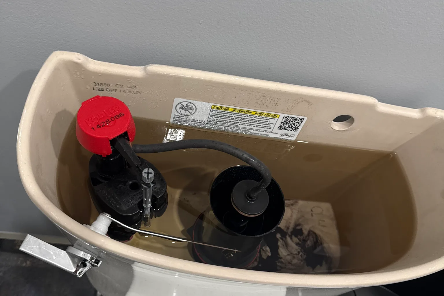Open toilet cistern showing a newly fitted red-capped Kohler fill valve and flapper