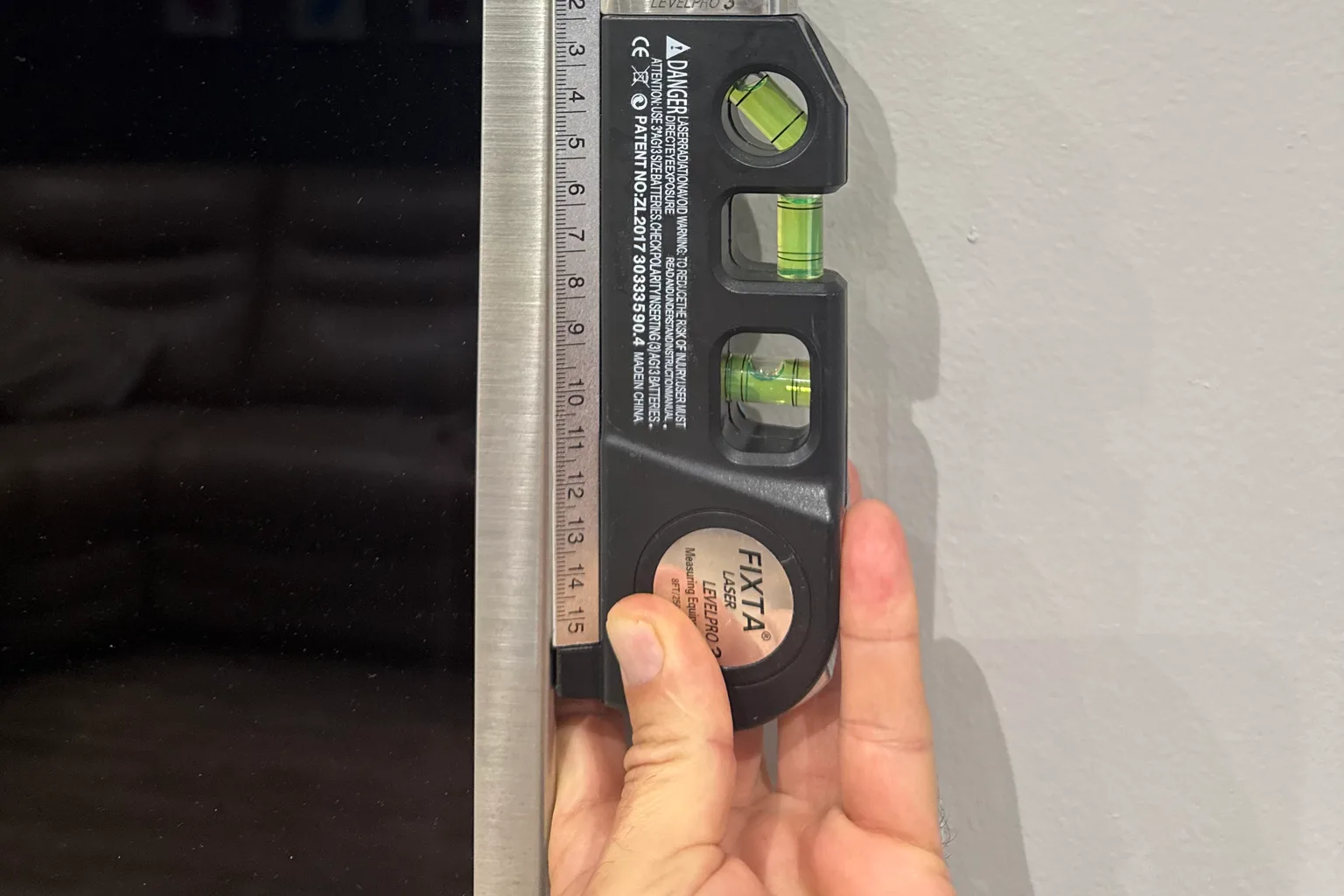 Laser level held against the edge of a wall-mounted television to check it sits level
